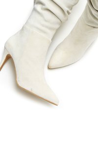 Weiße Wildleder-Ankle Boots mit spitzem Zehenbereich und dünnem Stiletto-Absatz, ausgestattet mit einem gerafften Schaft, der über den Knöchel reicht.