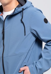 Chaqueta azul con cierre de cremallera en la parte frontal, capucha ajustable, bolsillos laterales y detalles en negro. El material es suave con un ligero brillo.