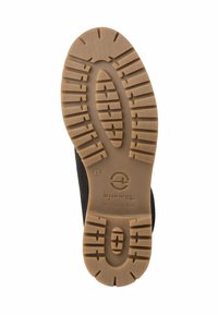 Semelle d'une chaussure noire avec une semelle extérieure en caoutchouc beige. Elle présente une texture antidérapante avec de profonds cannelures et une empreinte de logo ronde près du centre.