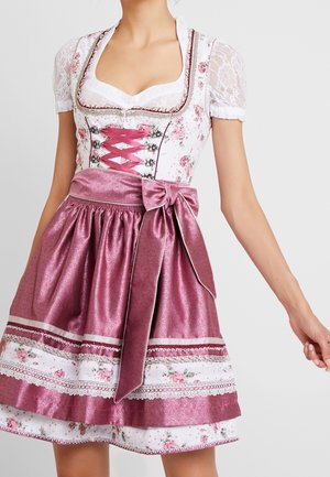 Kvinde iført en traditionel dirndl-kjole med lyserødt satinskørt, stor sløjfe, blomstrende korsettop, blondes ærmer og korsbånd foran.