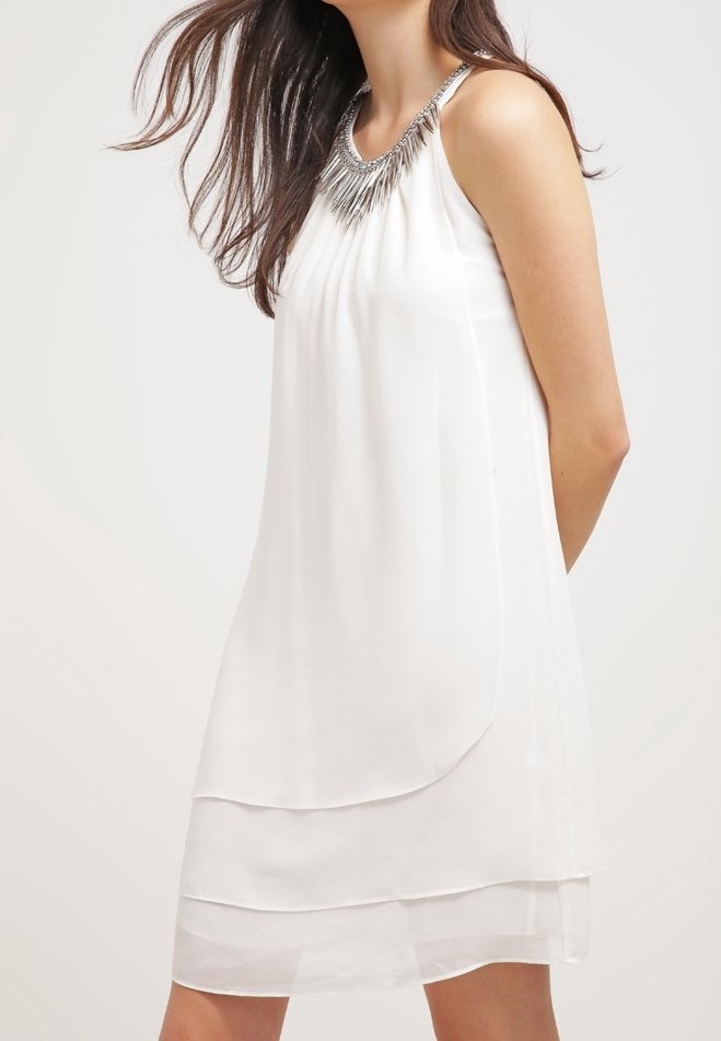 Vit ärmlös klänning med ett lagerdesign och ett silverfärgat metallhalsband vid halsringningen. Tillverkad av mjukt, lätt tyg.