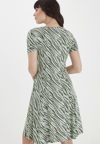 Kortærmet kjole i et grøn- og mintfarvet zebra-stribemønster, lavet af blødt stof med en blød skulder og en rund udskæring.