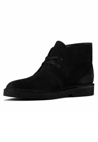 Black suede ankle boots featuring a laced design, rounded toe, and a flat rubber sole. Stitch detailing along the sole adds a subtle accent.