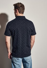 Pánská černá polokošile s krátkým rukávem, zdobená geometrickým vzorem v světle modré barvě. Hladká látka, límeček a rovný lem.