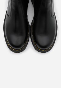 Stivali in pelle nera con punte arrotondate, caratterizzati da cuciture gialle a contrasto lungo la suola e una finitura liscia. Design elegante e resistente.