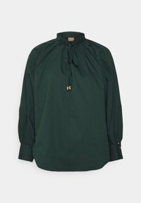 Blouse à manches longues vert foncé avec col montant, détails à cordon de serrage et accents dorés au niveau de l'encolure et des poignets. Texture lisse.