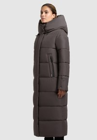 Long, padded coat in dark gray fabric, featuring a high collar, vertical zip pocket, and quilted design for insulation and warmth.