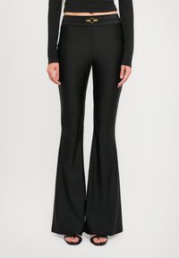 Black flared pants with a smooth, shiny texture. Features a wide waistband with a gold circular hardware accent at the front.