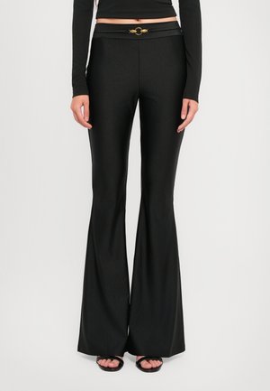 Black flared pants with a smooth, shiny texture. Features a wide waistband with a gold circular hardware accent at the front.