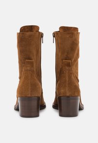 Bottes basses en daim marron avec fermeture éclair, talon en bois empilé et design légèrement froissé. Vue arrière mettant en valeur les coutures détaillées.