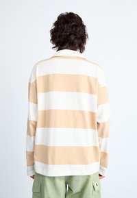 Långärmad skjorta i krämfärgade och ljusbeige ränder, tillverkad av mjukt bomull. Har en avslappnad passform och en klassisk kragdesign.