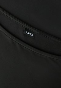 Schwarzer Stoff mit glatter Textur und dicht gewebtem Muster. Das "LMTD"-Etikett ist in Weiß auf schwarzem Hintergrund sichtbar.