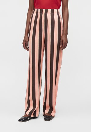 Personne portant un pantalon ample avec de larges rayures verticales rose et marron foncé, associé à des chaussures plates noires avec des détails métalliques.