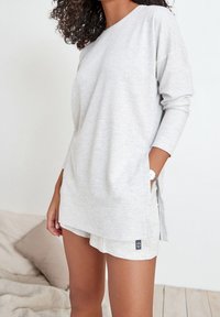 Haut à manches longues gris clair avec un motif texturé et des poches latérales, assorti à un short. Tissu doux avec une coupe décontractée.