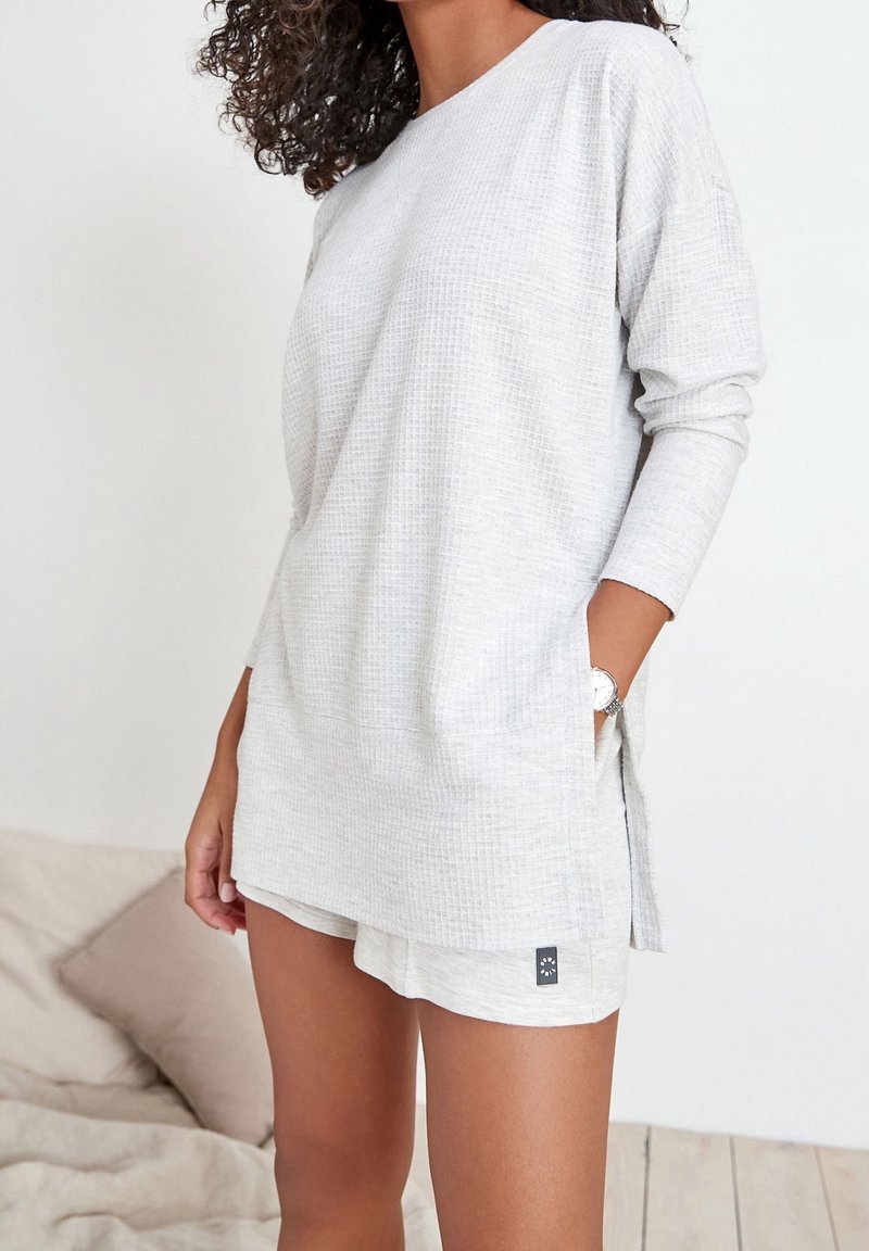 Haut à manches longues gris clair avec un motif texturé et des poches latérales, assorti à un short. Tissu doux avec une coupe décontractée.