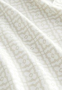 Bomuldsstof med et indviklet geometrisk mønster i beige på en hvid baggrund, der viser en glat tekstur og en subtil skær.
