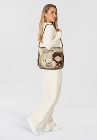 Beige Schultertasche mit Cartoon-Design, das ein Mädchen und den Text „Be yourself“ zeigt, ergänzt durch braune Akzente und verstellbaren Riemen.