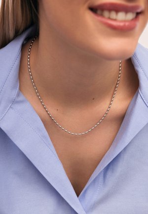 Silberne Perlenkette, die auf dem Schlüsselbein ruht, kombiniert mit einem hellblauen Hemd mit Kragen, das eine glatte Textur und ein einfaches Design zeigt.