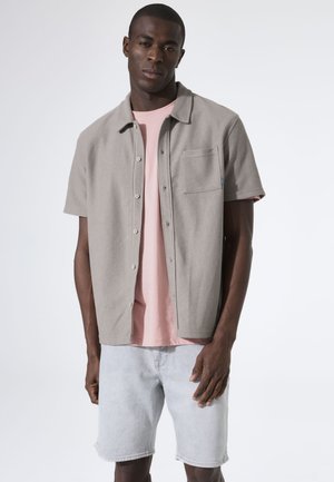 Graues kurzärmliges Hemd mit Kragen und Tasche, über einem pinken T-Shirt getragen, kombiniert mit hellgrauen Denim-Shorts. Glatte Textur und lässiges Design.