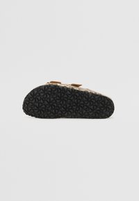 Brune slip-on sandaler med en mønstret sort gummisål, der har to justerbare remme og et blødt tekstureret overmateriale.