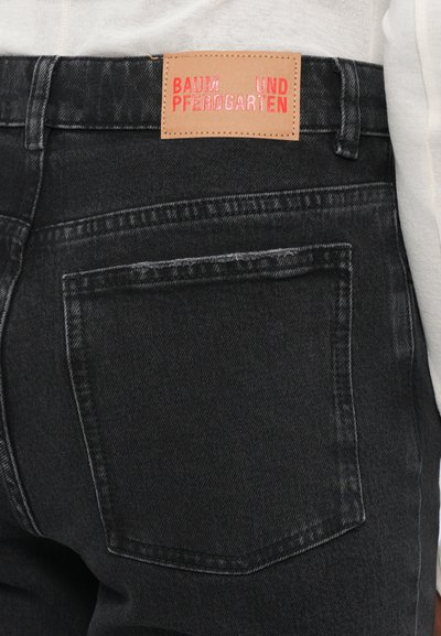 Black denim jeans with a high waist, featuring a brown leather label with embossed red text. Includes back pockets and subtle fading.