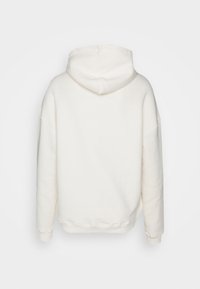 Sudadera blanca con capucha, de textura suave, corte holgado y hombros caídos. La parte trasera presenta un diseño simple y sin marcas visibles.