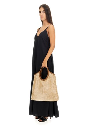 Sac fourre-tout beige texturé avec des accents marron, porté par un mannequin dans une robe noire. Le sac présente des anses robustes et un design spacieux.