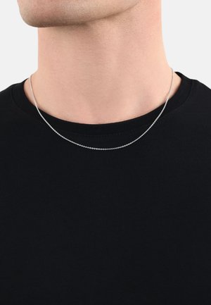 Collana in argento con un design delicato a catena, appoggiata su un collo nudo sopra una t-shirt nera a girocollo.