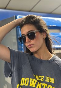 Ochelari de soare cu lentile întunecate și rame rectangulare clare. Hanorac casual gri cu text galben, purtat sub părul de lungime medie.