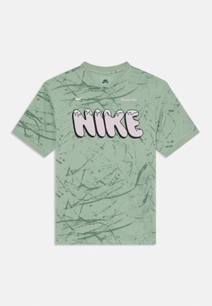 Camiseta de algodón verde con un diseño texturizado. Presenta un gran logo de "NIKE" en color rosa con un efecto de goteo y un pequeño texto de "Skateboarding" encima.