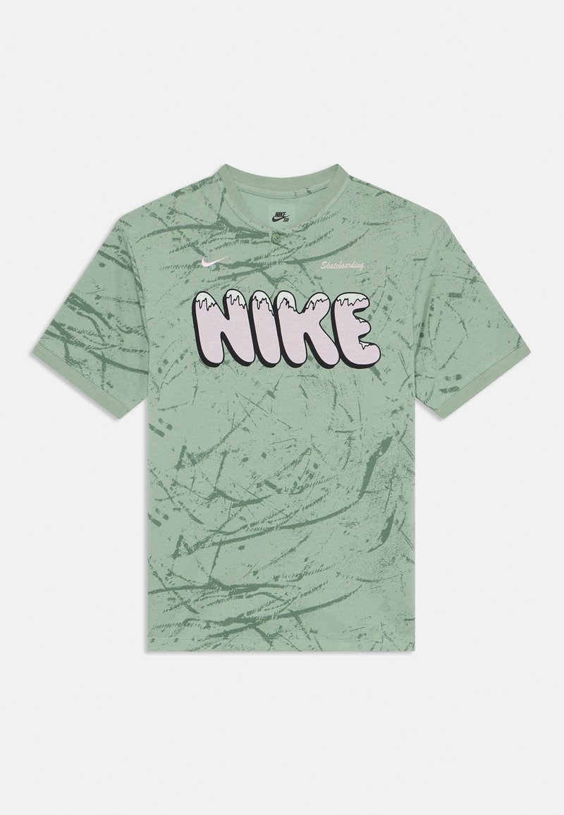 Camiseta de algodón verde con un diseño texturizado. Presenta un gran logo de "NIKE" en color rosa con un efecto de goteo y un pequeño texto de "Skateboarding" encima.