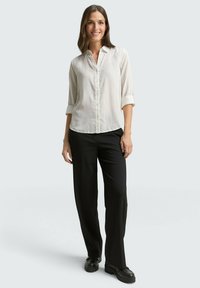 Chemise blanche à manches retroussées, associée à un pantalon noir à jambes droites. Tissu lisse, coupe décontractée et design simple.
