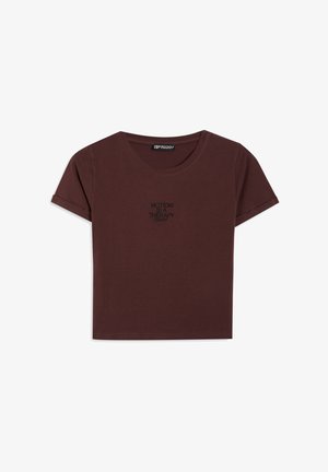 T-shirt bordeaux a maniche corte in cotone con scollatura tonda e maniche arrotolate; presenta la scritta nera "MOTION IS A THERAPY" sul davanti.