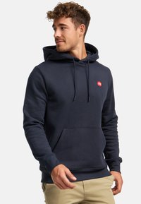 Sudadera azul marino hecha de tejido suave, que cuenta con un bolsillo tipo canguro y un pequeño logo rojo en el pecho, con capucha ajustable.