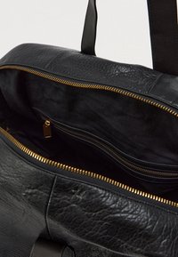 Melnas ādas soma ar rāvējslēdzēja aizdari, ar gludu ārējo virsmu un zelta rāvējslēdzēju. Iekļauj iekšējo kabatu ar rāvējslēdzēju.