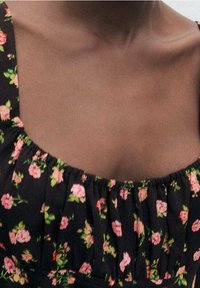 Musta kukallinen mekko, jossa on lyhyet röyhelöhihaiset hihat, joissa on vaaleanpunaisia kukkia ja vihreitä lehtiä; pehmeä, tekstuuriainen kangas neliönmuotoisella pääntie.