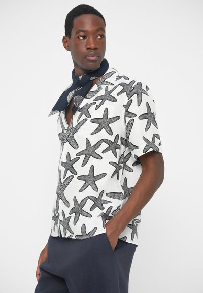 Kratke rokave, bela srajca z motivom črne morski zvezde. Ima izrezan ovratnik in udoben kroj. Nosi se z temno modrim šalom.