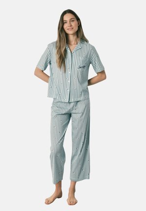 Kvinde står barfodet iført lyseblå, stribet to-delt pyjamas med små Snoopy-mønstre og korte ærmer.