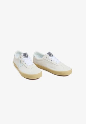 Para białych sneakersów Vans typu low-top z beżowymi podeszwami, białymi sznurówkami i logo "Vans Off The Wall" na języku, ukośnie na białym tle.