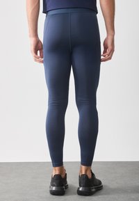 Tengerészeti színű sportleggings, testhezálló kialakítással, texturált anyagból és magas derékkal, fekete sportcipővel párosítva.
