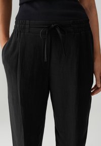 Pantalons noirs à coupe décontractée, taille élastique, fermeture à cordon, deux poches latérales et une texture douce et légère.