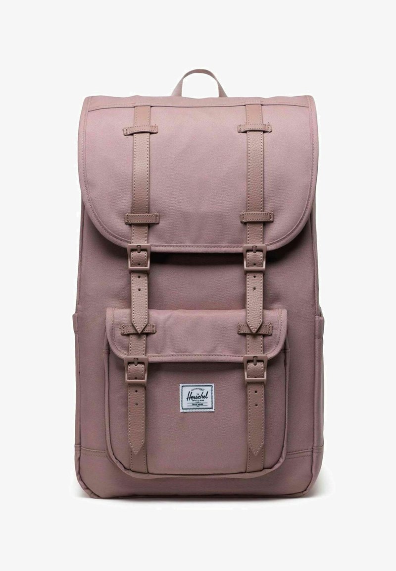 Sac à dos mauve avec des sangles de boucle à l'avant, fermeture à rabat, poche avant avec boucles et étiquette de marque Herschel sur la poche.
