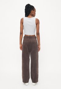 Grijze cropped tanktop gecombineerd met bruine wijde corduroy broeken. De broeken hebben een gestructureerde stof en achterzakken. Witte sneakers maken de look compleet.