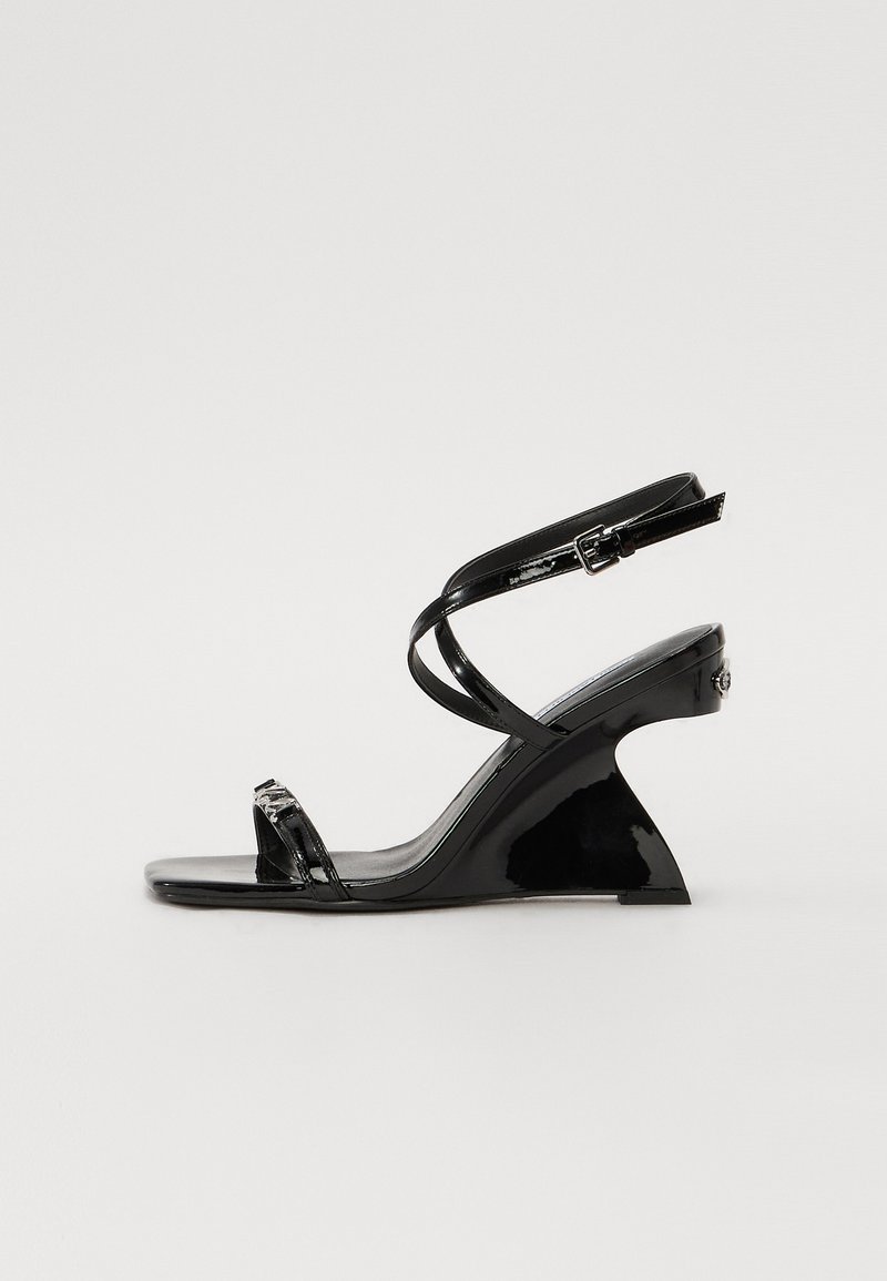 Sandale compensée en cuir verni noir avec un design élégant, à bout ouvert, des fines lanières à la cheville et une boucle décorative.