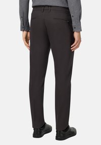 Męskie ciemno-brązowe spodnie z gładkiego, mieszane tkaniny. Dopasowany krój i dwie tylne kieszenie, noszone z czarnymi butami.
