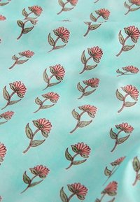 Tissu bleu clair avec un motif répétitif de petites fleurs roses avec des feuilles vertes et des tiges marron.