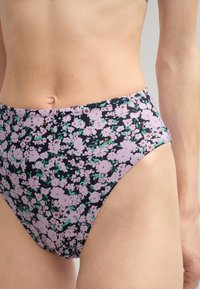 Bas de bikini taille haute avec un fond bleu marine présentant de petits motifs floraux roses et blancs. Fabriqué en tissu lisse et extensible.