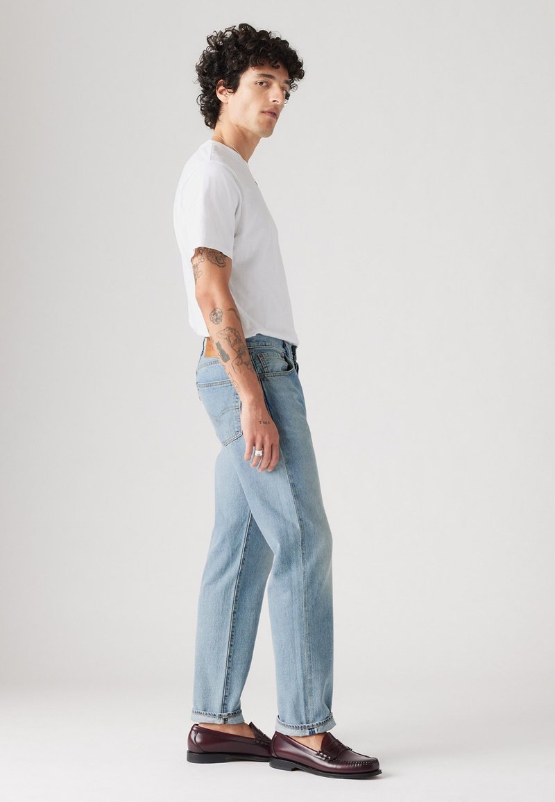 Jeans de mezclilla azul claro con un corte relajado, combinados con una camiseta blanca lisa. Dobladillo curvado notable y mocasines burdeos oscuros.