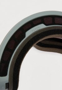 Közelkép a párnázott szélekről, amelyeken több habréteg található, és a "poc" logó dombornyomott egy ívelt szürke kereten.