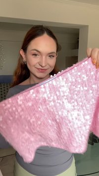 Ružový top s flitrami a textúrovanou tkaninou, s voľným strihom a okrúhlym švom. Flitre odrážajú svetlo a vytvárajú trblietavý efekt.